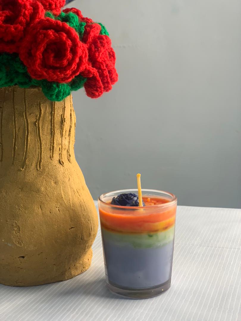 A layered rainbow candle beside a clay vase of crochet roses