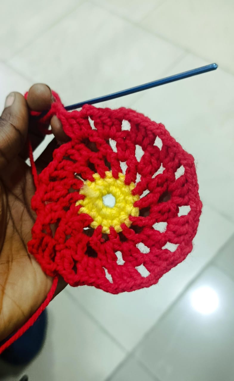 A red and yellow crochet round in progress, hook still in the work