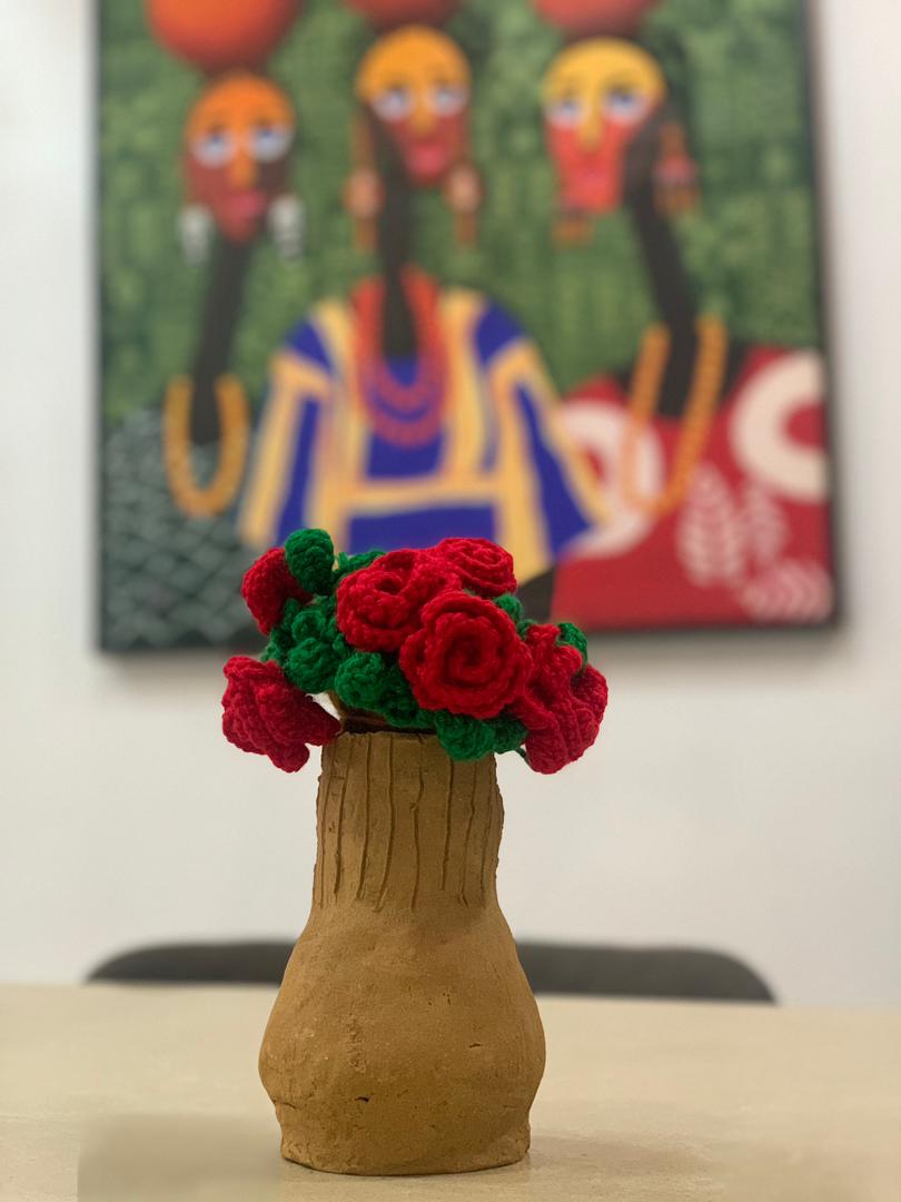 Crochet roses in a clay vase in front of a colourful painting