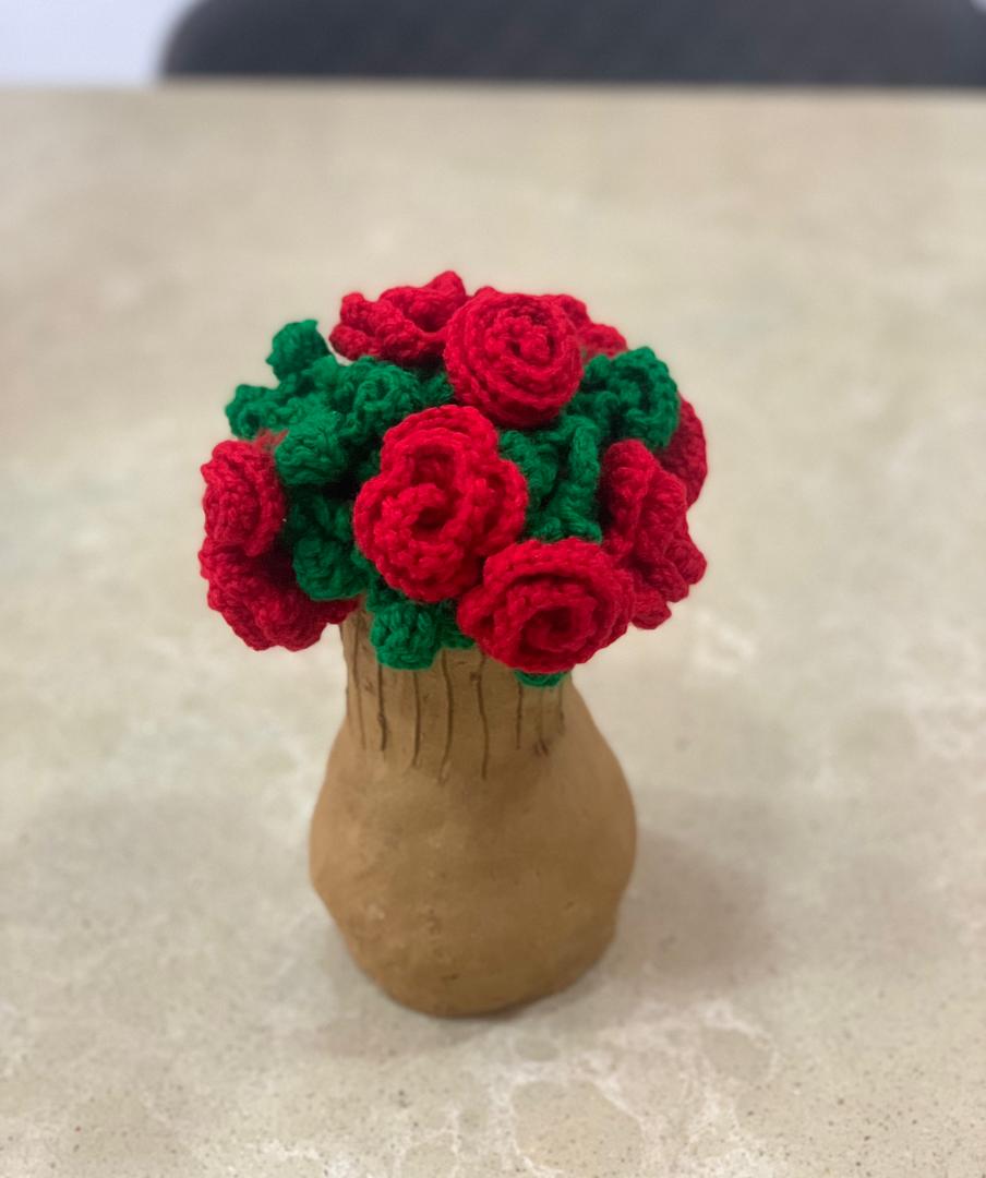 A bunch of red crochet roses with green leaves in a handmade clay vase